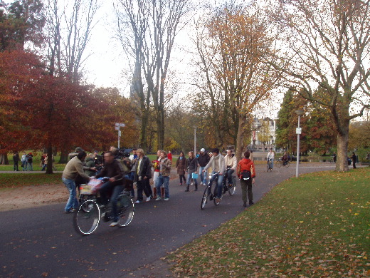 Half verborgen achter de fietsers loopt een processie artistieke mensen achter een filmploeg aan.