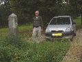 Bij naderende avondschemering Grenspaal 308 naast de auto aan Nederlandse kant.
