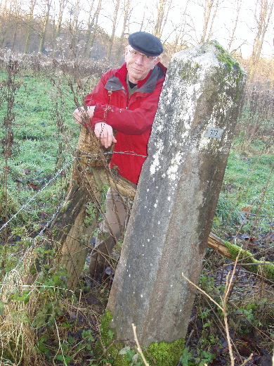 Iets verder op staat grenspaal 379 beschermd door prikkeldraad in een veld.
